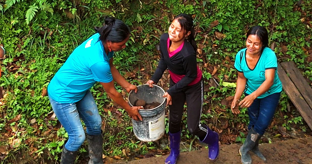 Three women of Verde Sumaco laughing as they pass a bucket of concrete