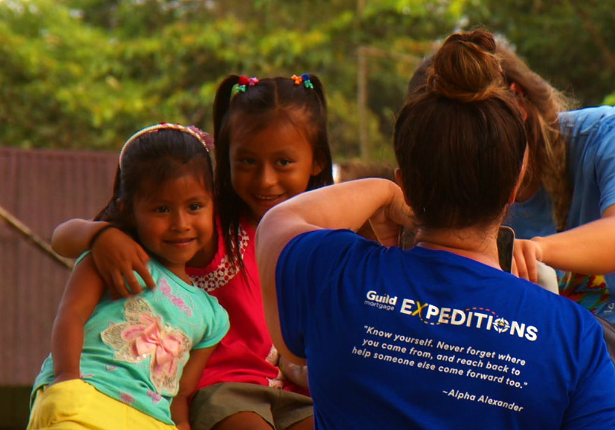 Two girls posing beside a volunteer in a Guild Expeditions shirt