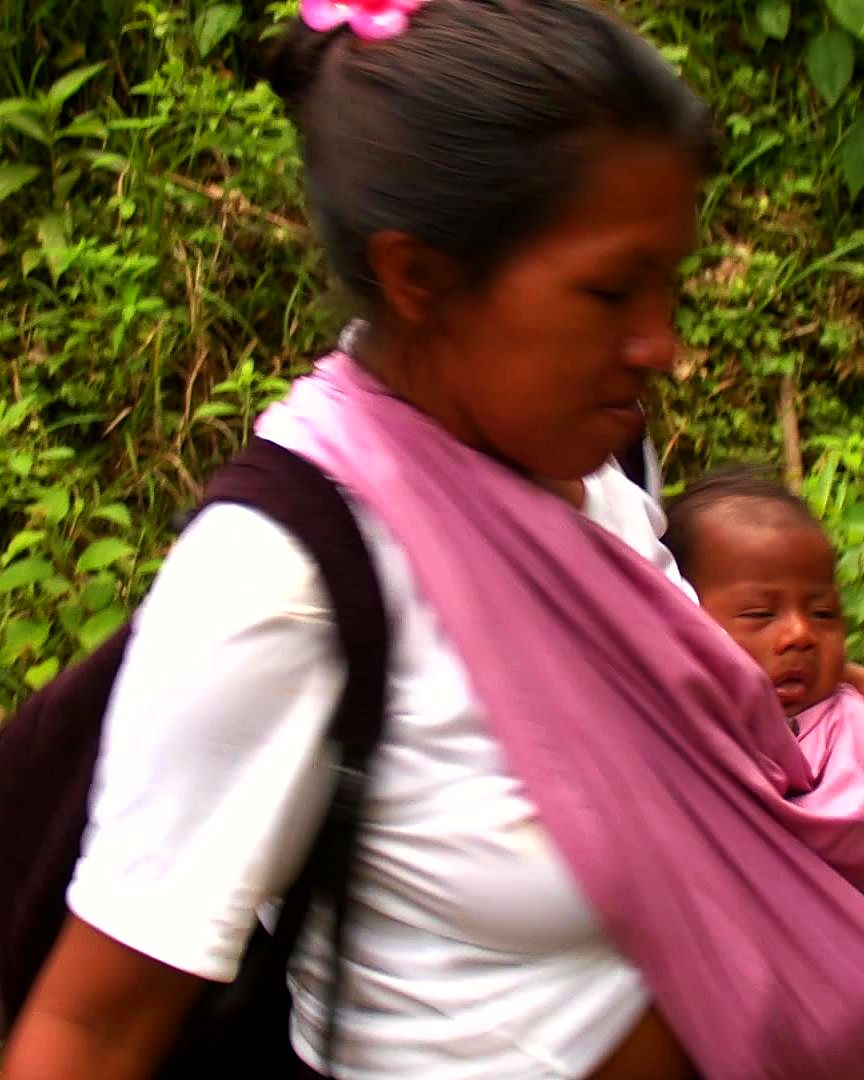A mother carrying her baby in a pink sling